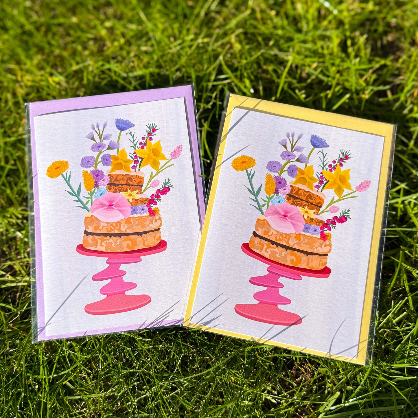 Two greeting cards with cake and flower designs on a grass background