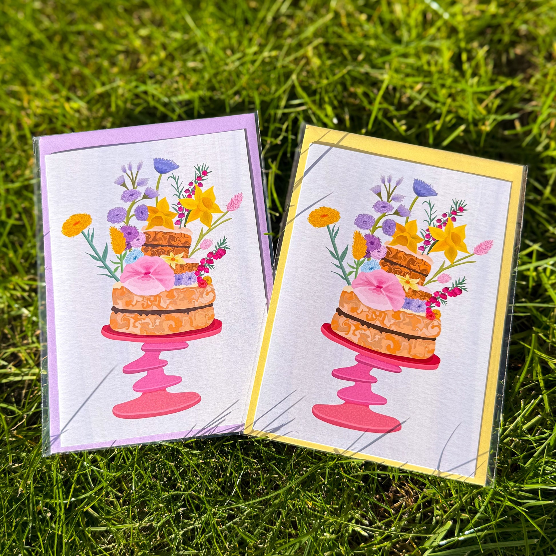 Two greeting cards with cake and flower designs on a grass background