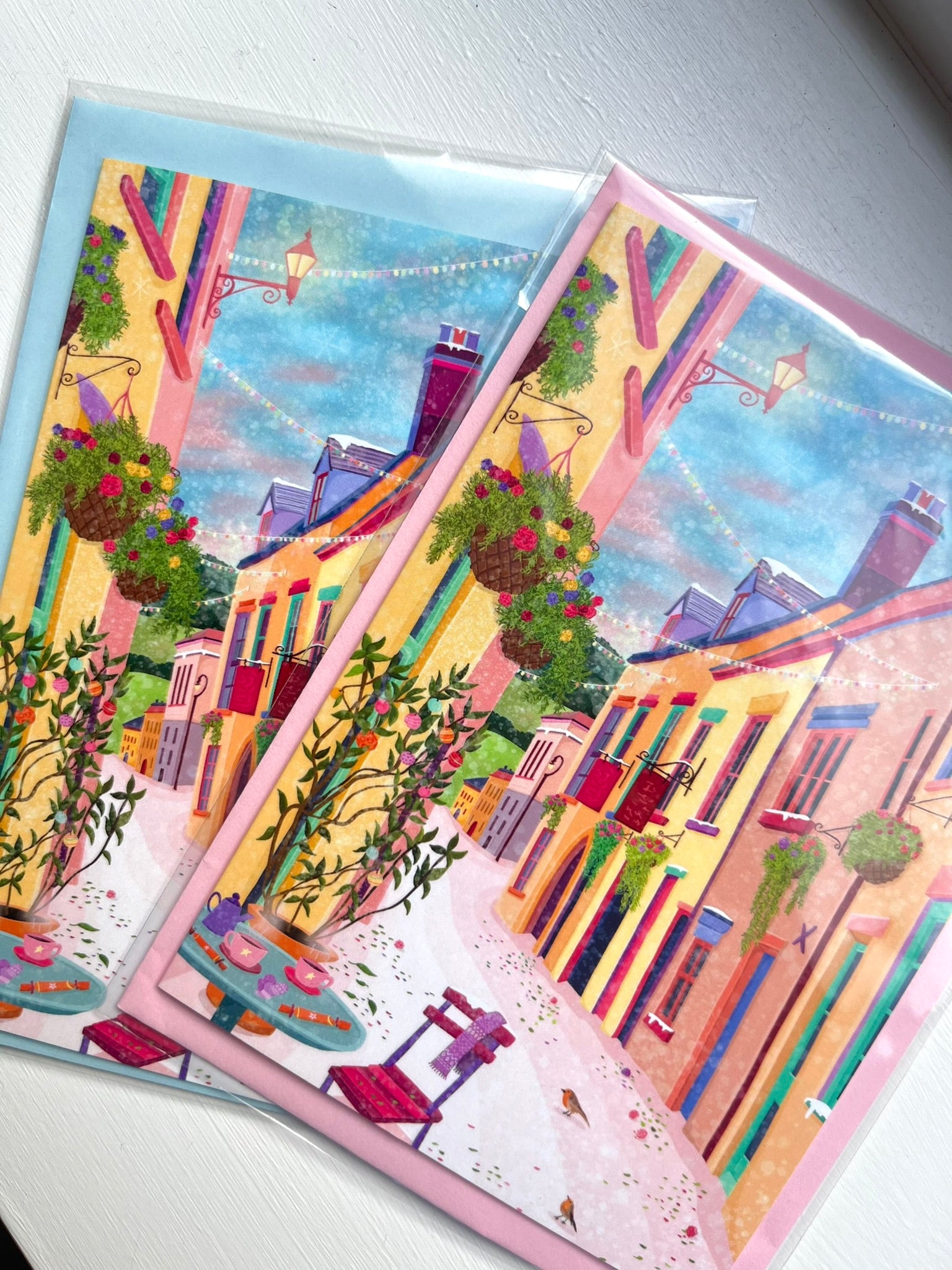Two colorful greeting cards with street scene illustrations on a white surface.